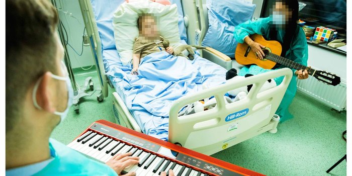Michał gra na&nbsp;instrumencie klawiszowym przy łóżku małego pacjenta, obok osoba z&nbsp;gitarą